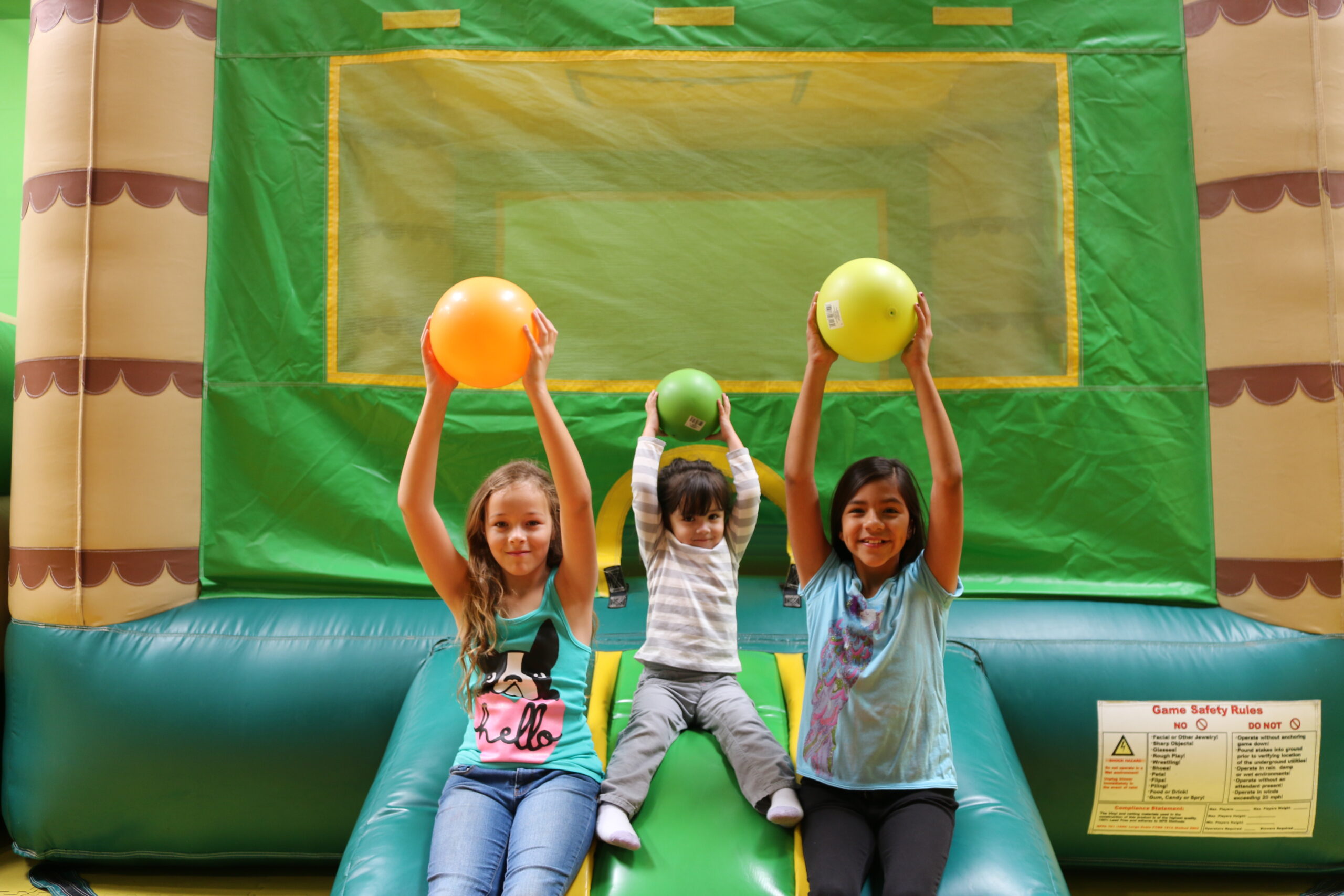 Three children playing in a bounce house with playballs.