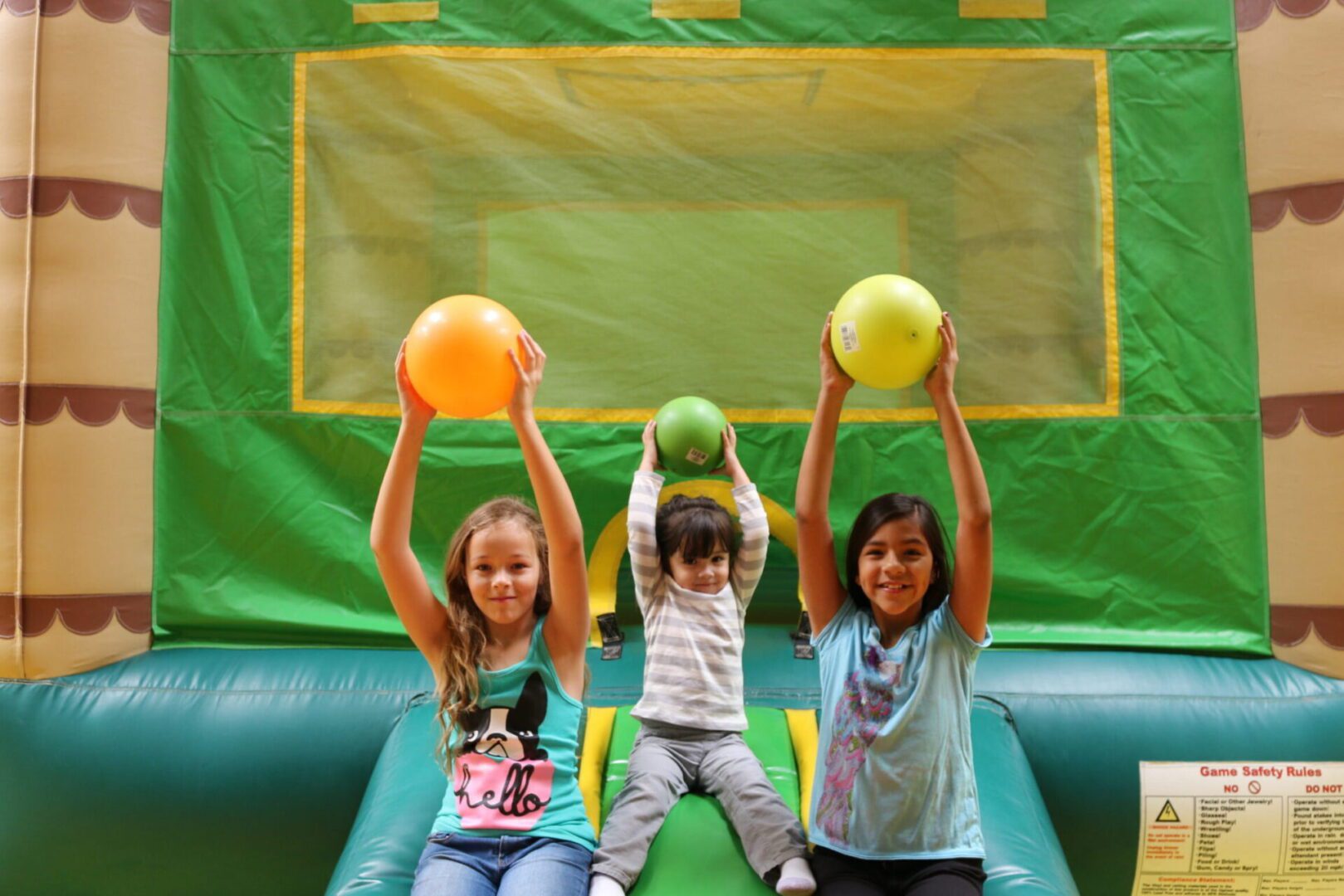 Three children playing in a bounce house with balloons.